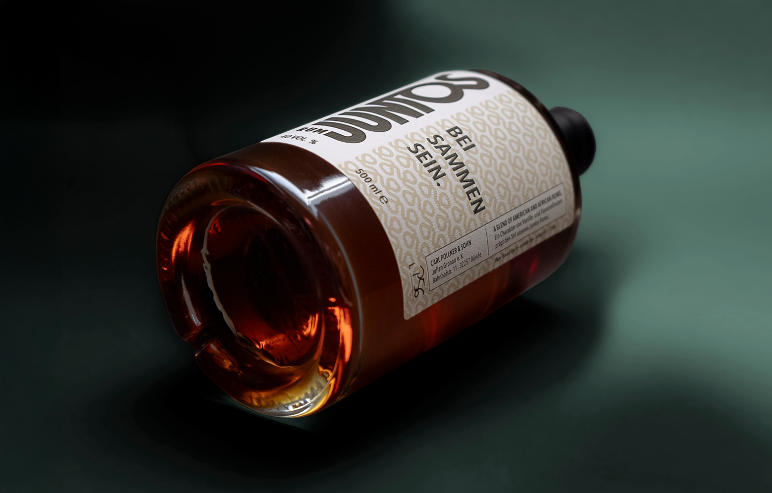 JUNTOS Rum Produktfoto. Eine Flasche liegend fotografiert in einem dunkelgrünen Setting.